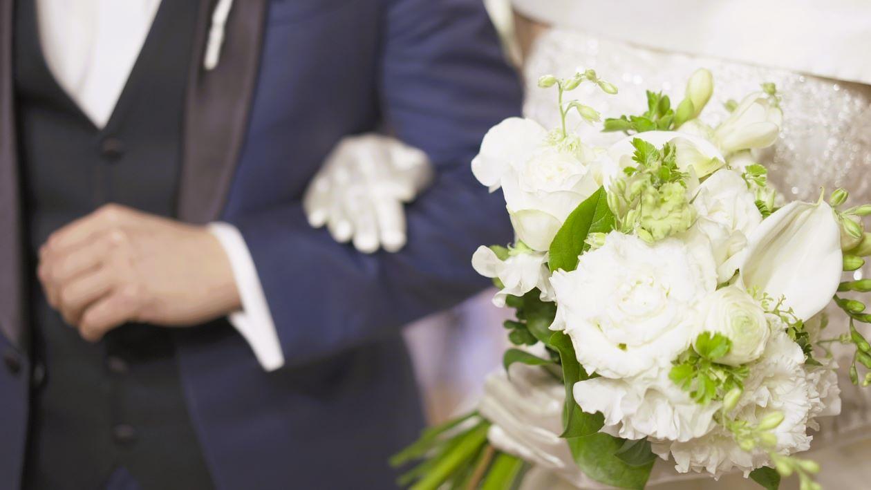 結婚式をあげた新郎新婦。新婦が新郎の腕に手をかけている。