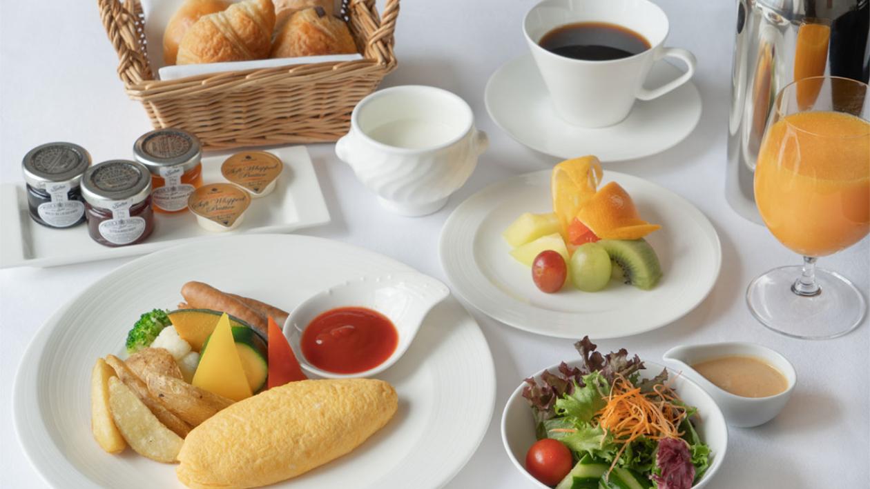 白いテーブルに並べられた洋朝食。オムレツを中心に、サラダ、フルーツ、パン、ジャム、コーヒー、オレンジジュースが彩りよく配置され、ホテルの朝食を思わせる上品で清潔感のある雰囲気が広がっている。