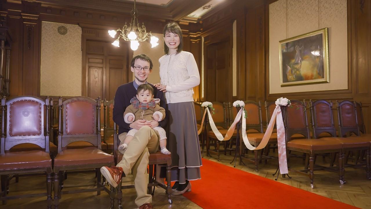 夫婦と赤ちゃんの三人がチャペルで座って記念撮影をしている。