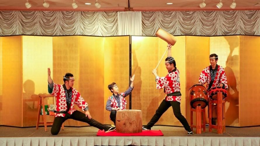 金屛風の前で、四人の演者による餅つきショーが行われている