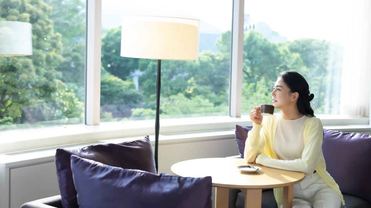 ザ・プリンス さくらタワー東京客室の窓辺から日本庭園を眺める女性客。