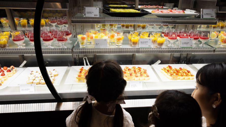 ショーケースに並ぶ色とりどりのデザートを選ぶこどもたち