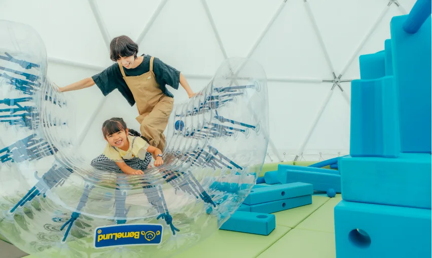 ドームテントの中でエア遊具に乗って遊ぶ子ども