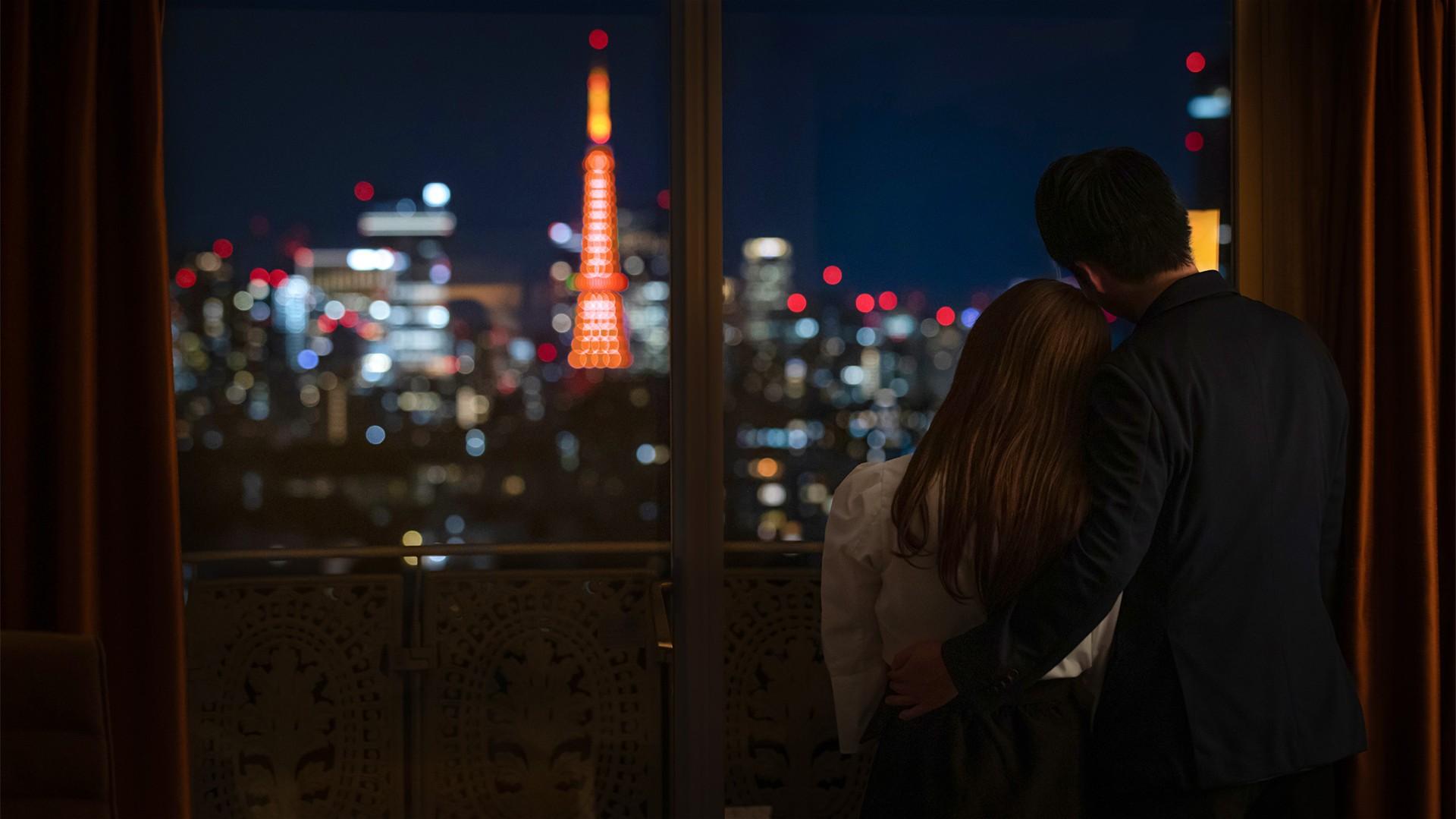 窓越しに見える夜の輝く東京タワーを寄り添って眺めふたり。